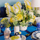 Decorative table setting with yellow and blue elements, including flowers and tableware.