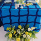 Blue tablecloth with white vases and plates with yellow flower arrangements