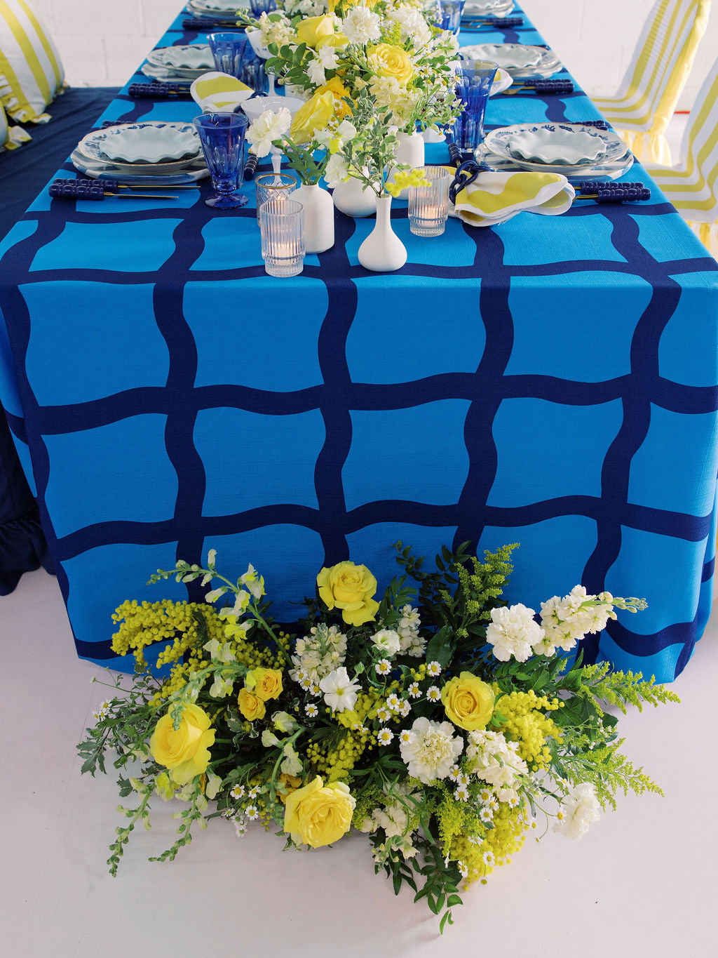 Blue tablecloth with white vases and plates with yellow flower arrangements