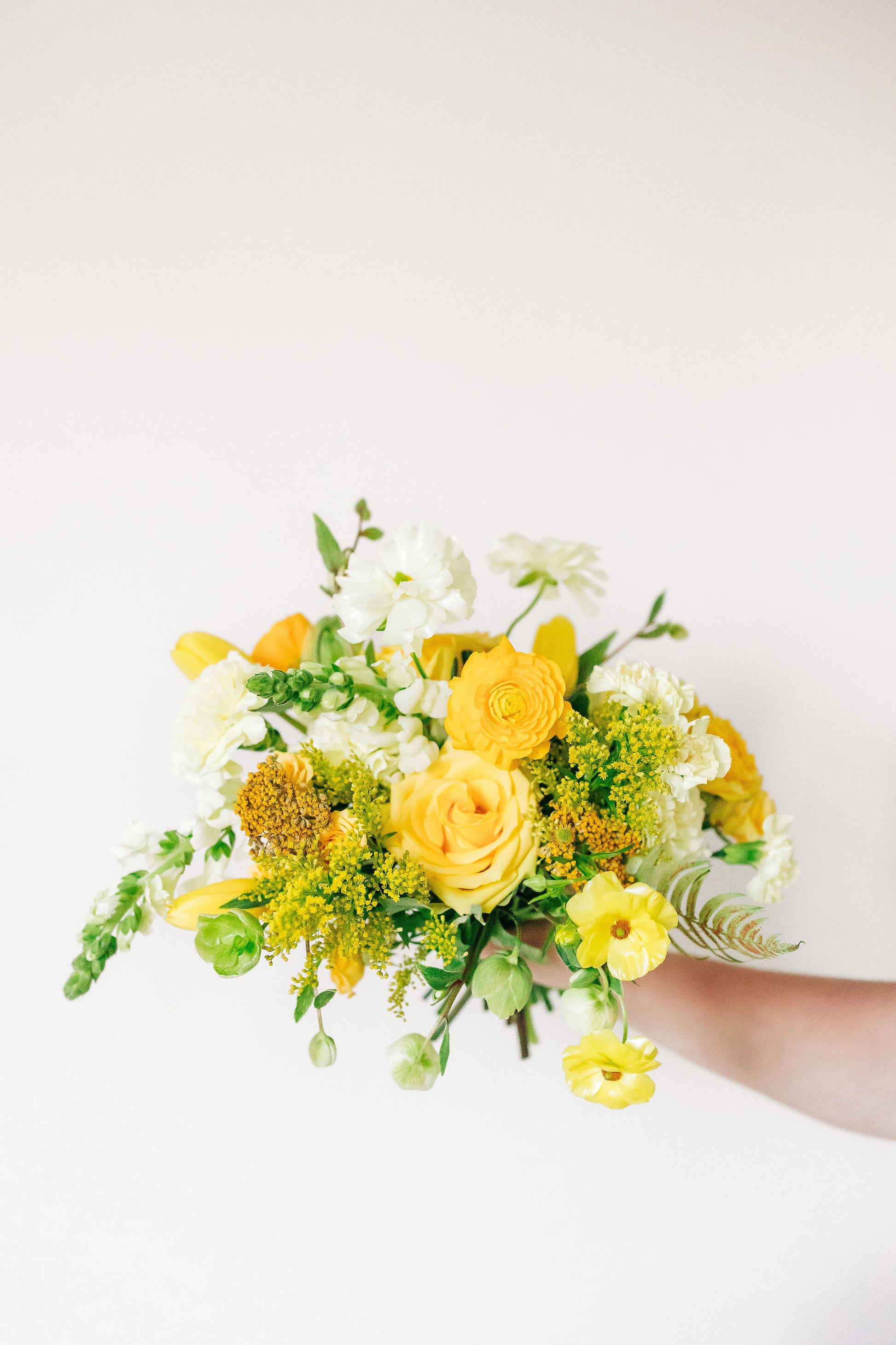 Bouquet of yellow and white flowers held by a person on a light background